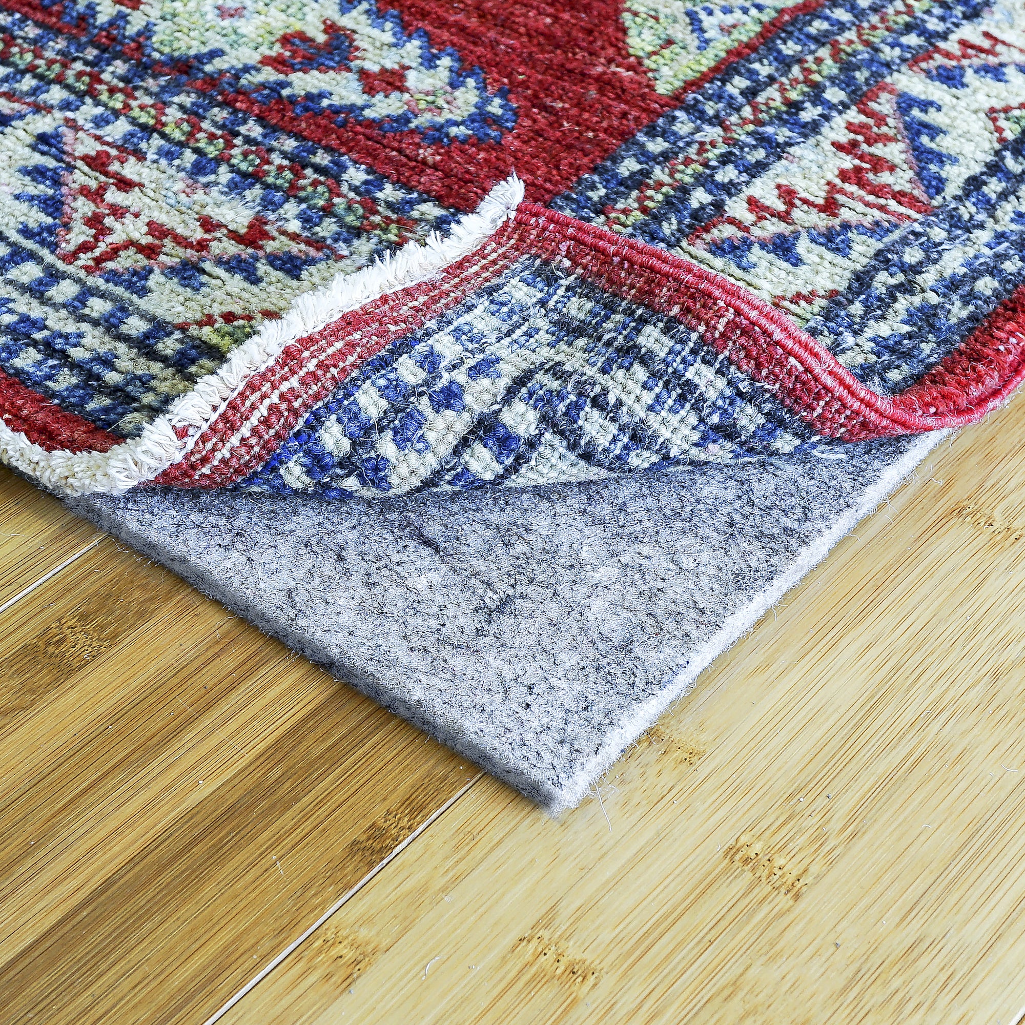 Lifestyle view of gray felt non-slip rug pad under corner of patterned rug on bamboo floor